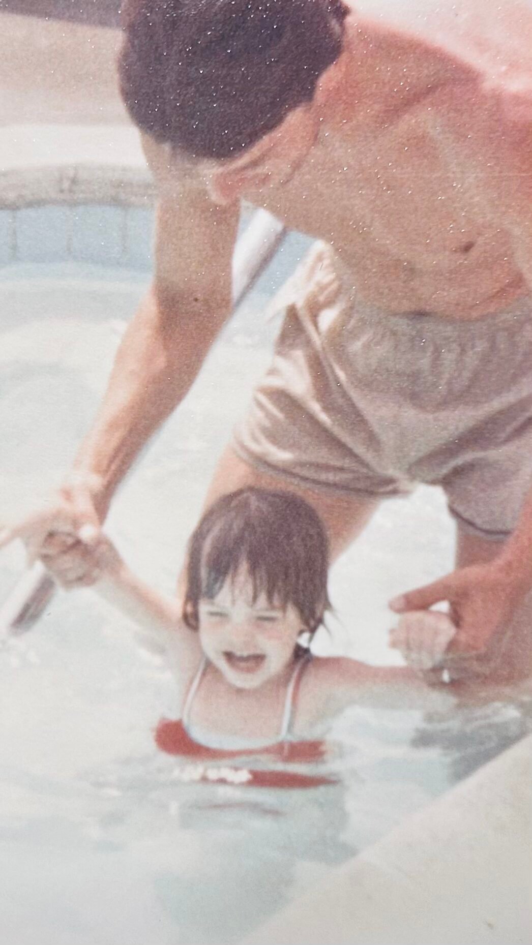Shannon at age 2 with her dad, Brandt in the pool. He is clutching her arms and holding her above the water. | Mr. Countertops